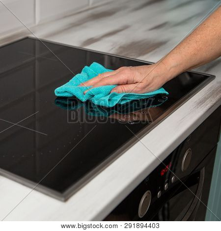 A Woman's Hand With A Blue Microfiber Cloth Rubs A Glass Ceramic Stove In The Kitchen.