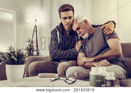 Heartsore Grandchild Hugging And Comforting His Elderly Silver-haired Granddad