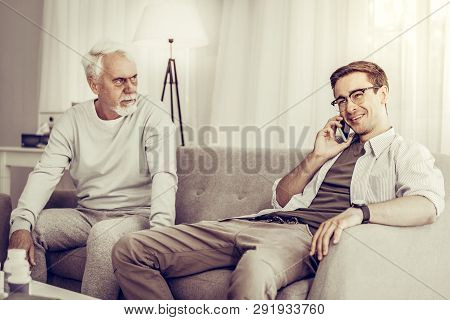 Young-adult Son Speaking Over Phone While Father Sitting On Sofa