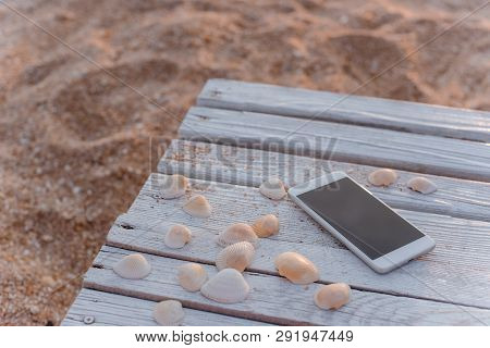 The Smartphone Lies In The Encircling Of Seashells On Wooden Boards.