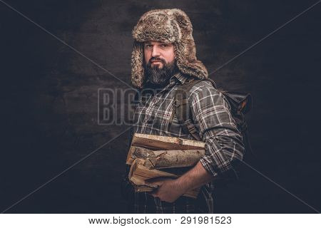 Portrait Of A Bearded Woodcutter With A Backpack Dressed In A Plaid Shirt And Trapper Hat Holding Fi