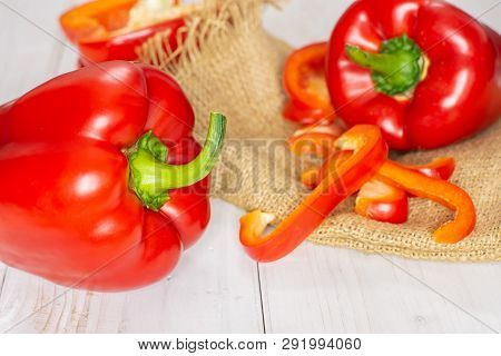 Group Of Two Whole One Half Four Slices Of Bulgarian Red Bell Pepper On Jute Cloth On White Wood