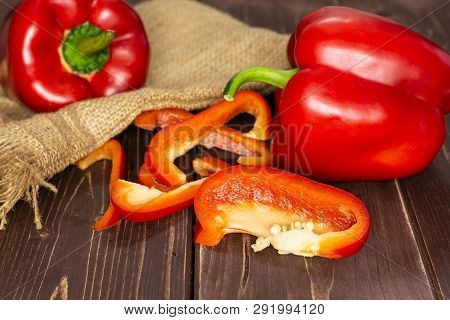 Group Of Two Whole Four Slices Of Bulgarian Red Bell Pepper On Jute Cloth On Brown Wood
