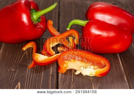 Group Of Two Whole Four Slices Of Bulgarian Red Bell Pepper On Brown Wood