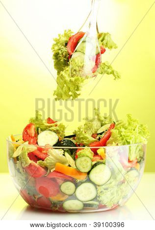 Frischer Gemüsesalat in transparente Schale mit Löffel und Gabel auf grünem Hintergrund