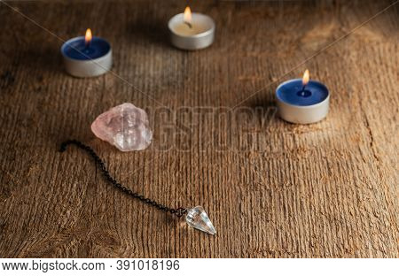 The Pendulum On A Chain With A Natural Crystal On A Background Of Wood Texture With Burning Candles.