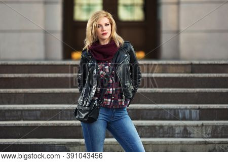 Young fashion blonde woman with handbag on city street  Stylish female model in black leather jacket and snood scarf