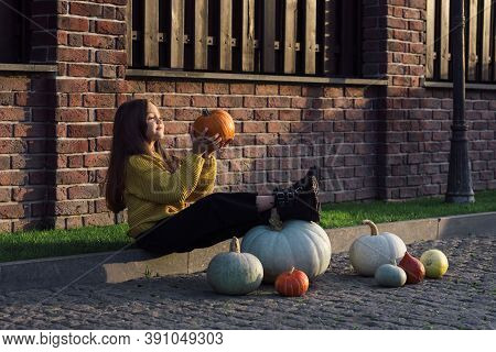 Funny Child Girl In Orange Pullover For Halloween With Pumpkin And On A Dark Brick Background.