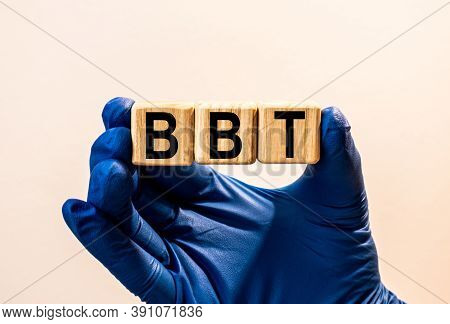 The Word Bbt Which Is Made From Wooden Cubes. Hands In A Blue Glove. Isolated On White Background.