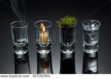 Four Elements Of Nature - Air, Fire,  Earth, Water. Four Elements Concept In Glasses On A Black Refl