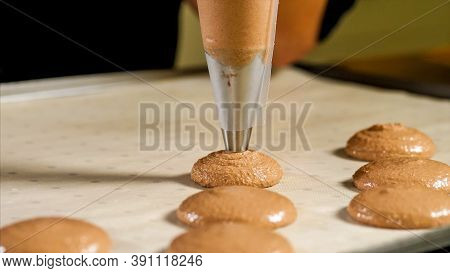Chef Making Base For Preparation Macaron Dessert. Close-up Of Extruding Brawn Creme From Piping Bag 