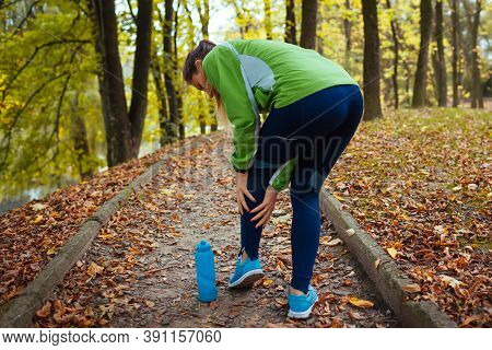 Young Runner Injured Leg During Workout Exercises In Autumn Park. Woman Feels Ankle Pain And Crick. 