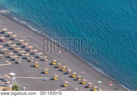 Kamari, Santorini Island, Greece- 19 September 2020: Black, Volcanic Beach Wit Chairs Lawn In Kamari