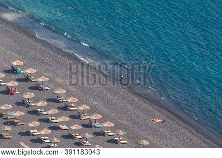 Kamari, Santorini Island, Greece- 19 September 2020: Black, Volcanic Beach Wit Chairs Lawn In Kamari