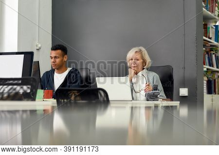 Aged Woman, Senior Intern Looking Uncertain At The Screen While Using Laptop, Sitting At Desk, Worki