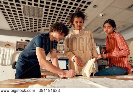 Creative People Making Notes, While Discussing Logo And Design Of T-shirt. Young Man And Women Worki