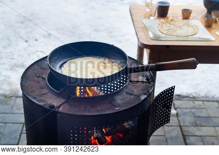 Cooking Pancakes On An Open Fire On An Iron Stove In The Form Of A Barrel In Winter On Shrovetide. A