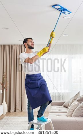 Man Cleaning Ceiling And Lamps In Living Room. House Cleaning Service Concept.