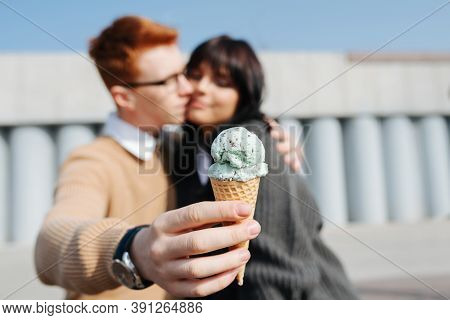 Blurred Image Of Couple Sitting Outdoors With Ice Cream, Kissing. Blurred Faces