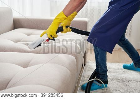 Close-up Of Housekeeper Holding Modern Washing Vacuum Cleaner And Cleaning Dirty Sofa With Professio