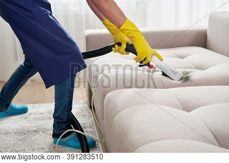 Close-up Of Housekeeper Holding Modern Washing Vacuum Cleaner And Cleaning Dirty Sofa With Professio