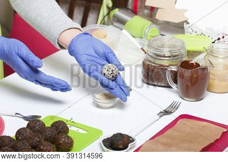 A Woman In Rubber Gloves Makes Candies From Dried Fruits And Nuts. Some Are Sprinkled With Sesame Se