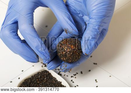 A Woman In Rubber Gloves Makes Candies From Dried Fruits And Nuts At Home In Self-isolation During A