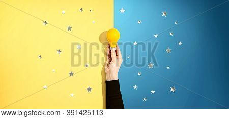 Person Holding A Yellow Light Bulb With Silver Shiny Stars