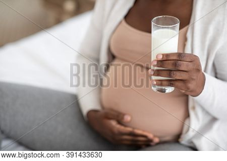 Pregnancy And Calcium. Black Expectant Mother Holding Glass Of Milk And Tenderly Embracing Belly, Pr
