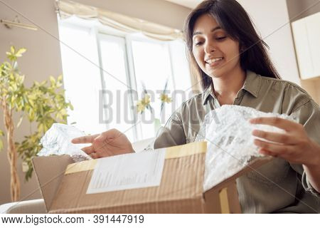 Smiling Indian Woman Shopper Customer Opening Post Package Box Sitting On Couch At Home. Happy Femal
