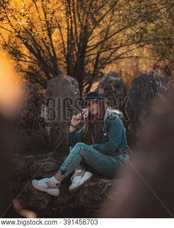 Portrait Of An Attractive Brunette Sitting In A Stone Well At The Rajcica Wells Landmark. Wearing Je