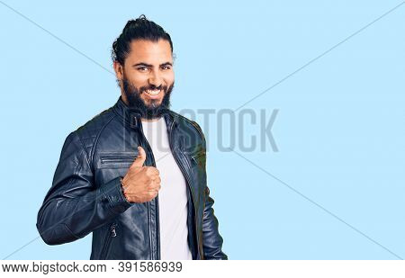 Young arab man wearing casual leather jacket doing happy thumbs up gesture with hand. approving expression looking at the camera showing success. 