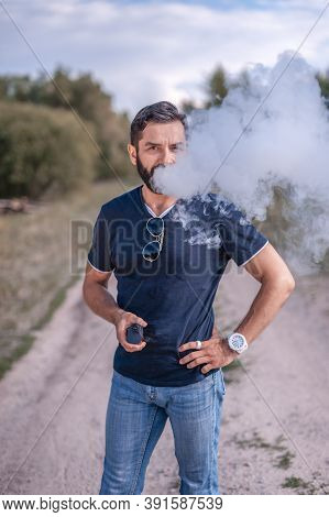 Bearded Vape Man Enjoying An Electronic Smoke Device In The Calm Outdoors. The New Technology Cigare