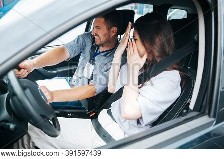 Male Driving Instructor Trying To Avoid A Collision With Another Car. Scared Young Woman Covers Her 