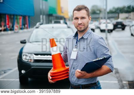 Male Driving Instructor Standing With Orange Traffic Cones And Clipboard In His Hands. Caucasian Man