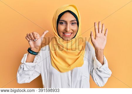 Young brunette arab woman wearing traditional islamic hijab scarf showing and pointing up with fingers number six while smiling confident and happy. 