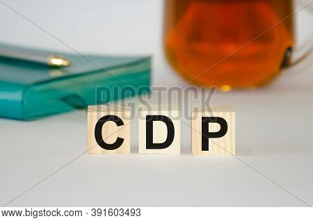 The Word Is Written On Wooden Cubes, In The Background Is A Notebook With Tea. The Word Cdp Is Prese