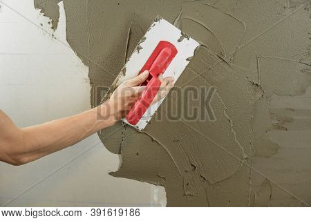 A Worker Plasters The Wall With A Spatula And Applies A Cement Mix Solution. The Repairman Lays The 