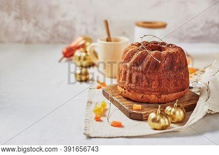Homemade Autumn Carrot Or Pumpkin Bundt Cake With Candied Fruits, Cup Of Tea And Golden Decorative P