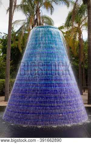 Blue Fountain With Smooth Water And Palm Trees Behind