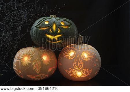 Green Pumpkin, Standing On Orange And White Pumpkins, All Three Carved On Dark Background