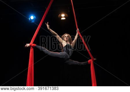 Young woman does aerial acrobatics with red fabrics