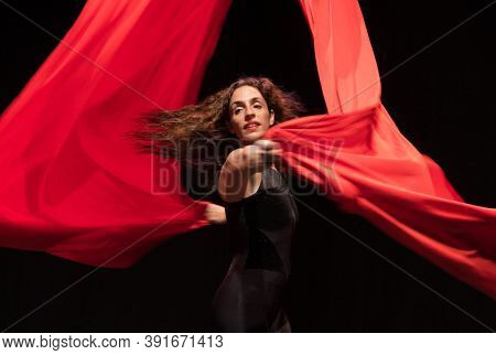 Young woman does aerial acrobatics with red fabrics