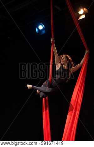 Young woman does aerial acrobatics with red fabrics