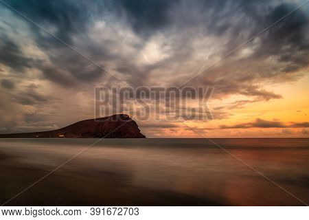 View Of A Beach And A Mountain At Sunset And A Sky With Clouds