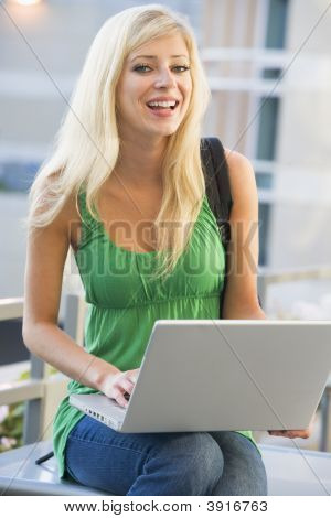 Kvinden sidder på bænken udendørs med Laptop smilende (selektiv fokus)