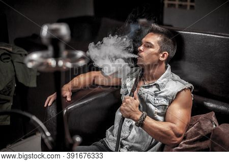 Handsome Man Blowing Clouds Of Smoke In The Hookah Bar.
