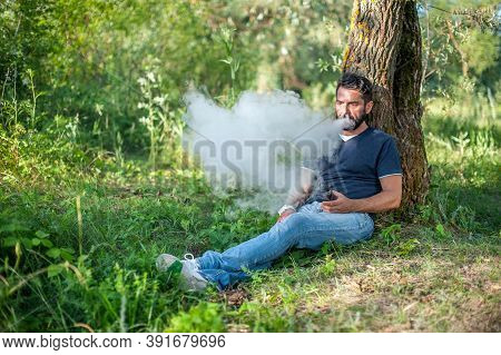 Stylish Bearded Vape Man Smoking An Electronic Smoke Device Out In The Forest. Vape.