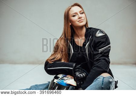 Cheerful And Cute Female Motorcyclist Poses Sitting On Floor With Her Helmet And Looking At Camear I