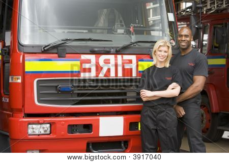 Dois bombeiros de pé na frente do motor de fogo